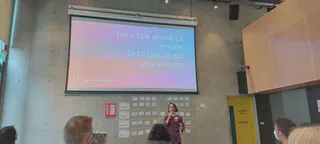 Fiona MacNeill is shown presenting to a large room, with the slide title projected above reading, Let&rsquo;s talk about LX maybe, Let&rsquo;s talk about you and me