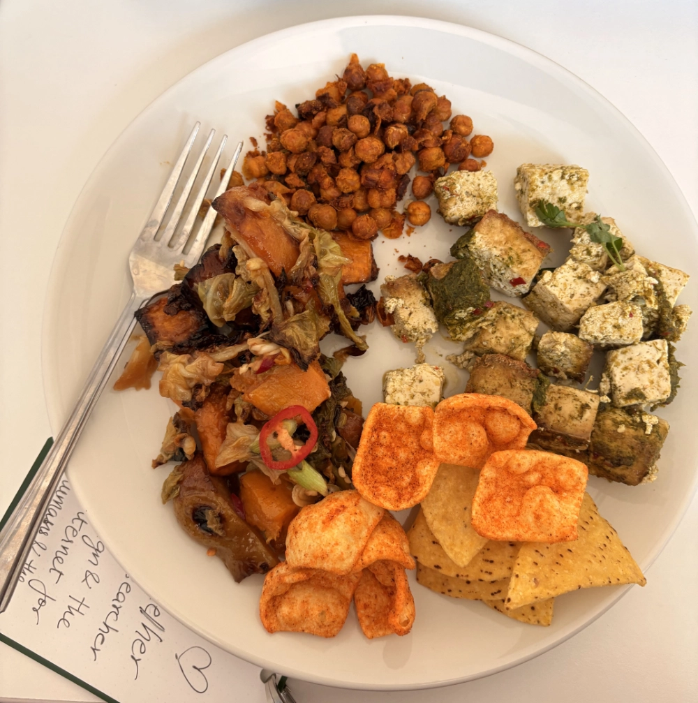 a plate of beautifully crafted food, including roasted aubergine, chickpeas, tofu, and some snack crisps for good measure.
