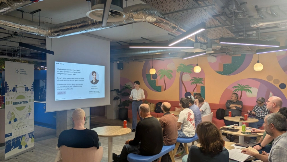 Runway East Brighton event space is pictured, filled with attendees. Fiona is standing at the front presenting a slide with informattion about Macknowlogist.